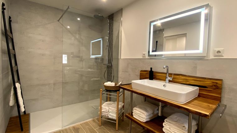 Ein modernes Badezimmer mit einer großzügigen, gläsernen Dusche und einem eleganten Waschbecken. Holzregale mit frischen Handtüchern runden das Gesamtbild ab.