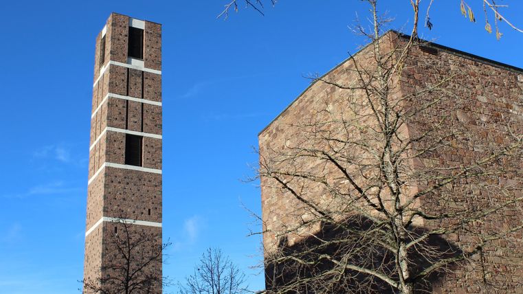 Ein hoher Turm aus Ziegelsteinen steht neben einem massiven Gebäude. Der Himmel ist klar und blau.