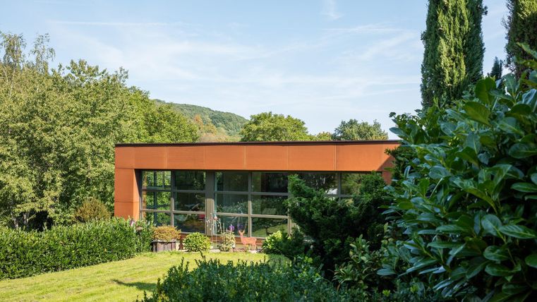 Ein modernes Haus mit großen Fenstern inmitten einer grünen Landschaft. Umgeben von Bäumen und gepflegtem Garten.