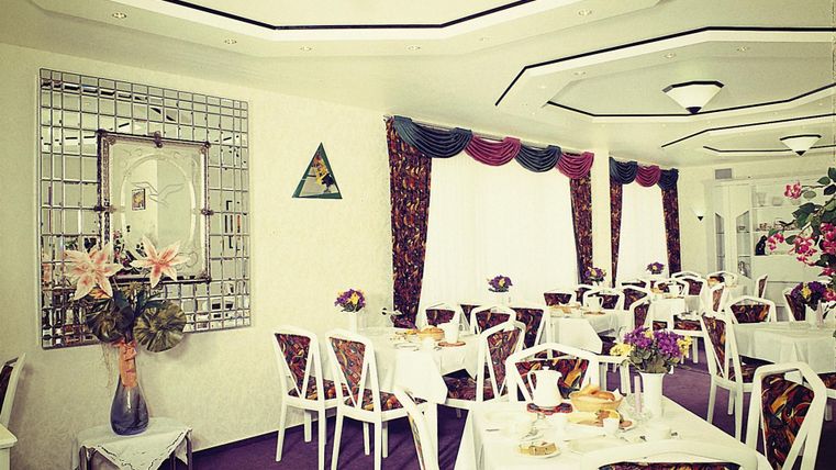 Ein elegantes Restaurant mit weißen Tischen und bunten Stühlen. Die Wände sind geschmackvoll dekoriert, und es gibt schöne Blumenarrangements auf den Tischen.