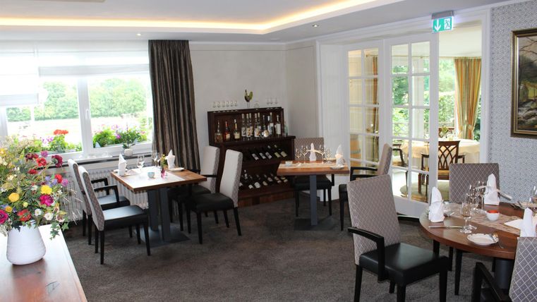 Ein elegantes Restaurant mit stilvoll gedeckten Tischen. Große Fenster lassen viel Tageslicht herein und bieten einen Blick ins Freie.