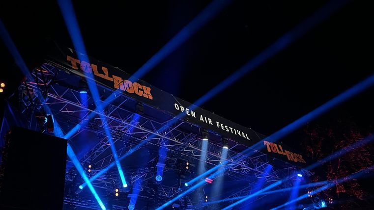 Eine Bühne bei einem Open-Air-Festival mit bunten Lichtern. Der Himmel ist dunkel, und die Atmosphäre ist festlich.