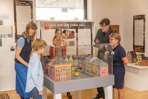 Eine Gruppe von fünf Personen steht um ein Modell von Gebäuden. Sie betrachten interessiert die Details des Modells in einem Ausstellungsraum.