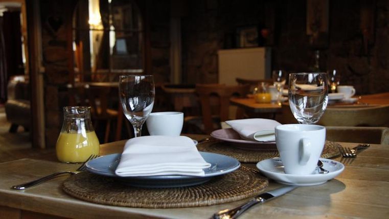 Ein gedeckter Tisch mit Tellern, Gläsern und Besteck in einem gemütlichen Restaurant. Im Hintergrund sind weitere Sitzplätze und eine entspannte Atmosphäre zu sehen.