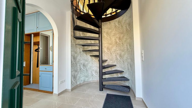 Eine moderne Treppe in einem hellen Eingangsbereich. Die Wände sind schlicht und die Böden sind mit hellen Fliesen ausgelegt.
