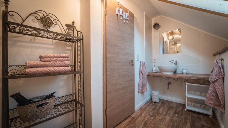 Ein modernes Badezimmer mit einem Holzregal und handtüchern. Es gibt einen Waschplatz und eine große Tür, die natürlichen Licht hereinscheinen lässt.