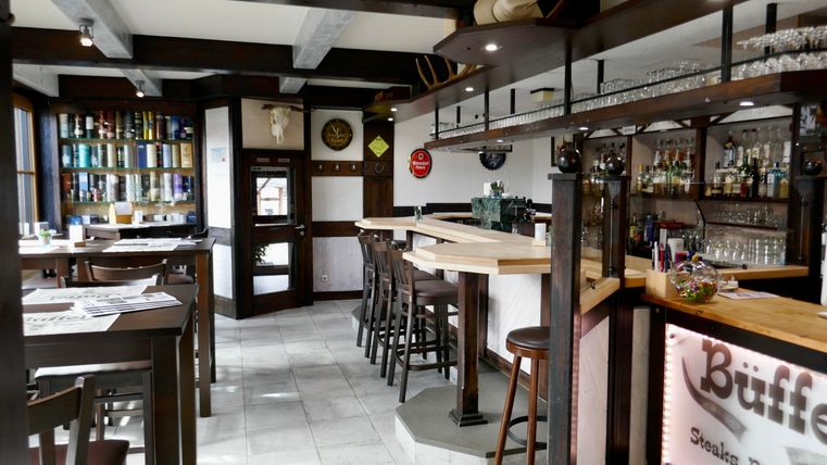 Ein gemütliches Restaurant mit einer Holzbar und modernen Möbeln. Die Wände sind dekoriert und der Raum ist hell und einladend.