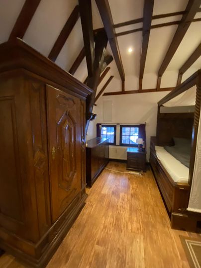 Ein gemütliches Schlafzimmer mit Holzboden und sichtbaren Deckenbalken. Es gibt einen großen Schrank und ein Bett in einem rustikalen Stil.