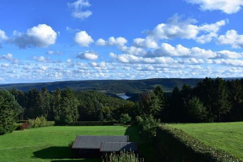 Eine malerische Landschaft mit grünen Wiesen und Bäumen. Der Himmel ist blau, und weiße Wolken schweben darüber.