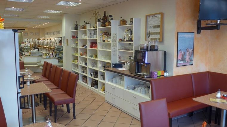Ein gemütliches Café mit roten Sitzbänken und Tischen. Im Hintergrund sind Regale mit verschiedenen Produkten und eine Theke zu sehen.