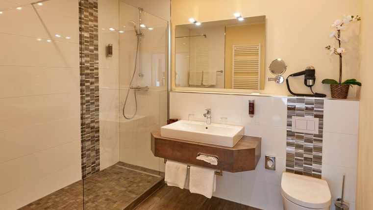 Ein modernes Badezimmer mit einer eleganten Dusche und einem Holzwaschtisch. Die Wände sind in hellen Farben gehalten und es gibt dekorative Elemente wie eine Orchidee.