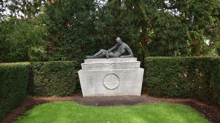 Eine Statue von zwei Figuren, die in einem gepflegten Garten aus Grün und Hecken stehen. Der Rasen ist gut gewachsen und die Umgebung ist ruhig und einladend.