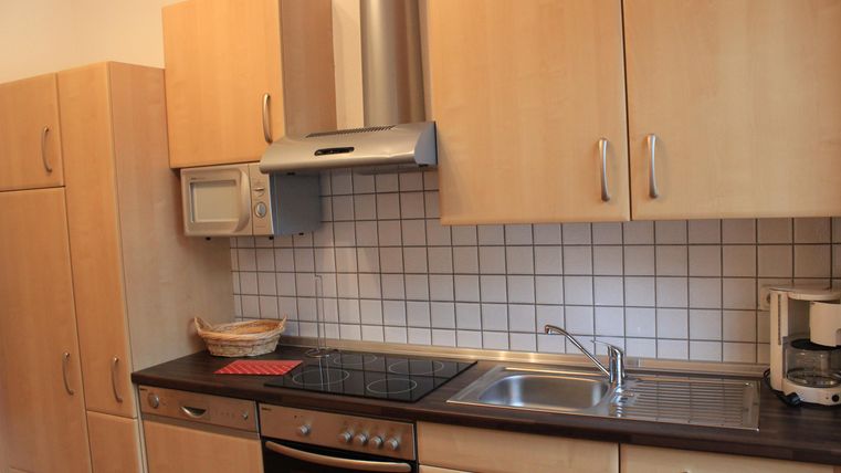Eine moderne Küche mit Holzschränken und einer Edelstahl-Spüle. Es gibt einen Herd, eine Mikrowelle und einen Kühlschrank.