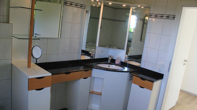 Ein helles Badezimmer mit einem modernen Waschbecken und einem großen Spiegel. Die Wände sind gefliest und die Einrichtung ist in Weiß und Schwarz gehalten.