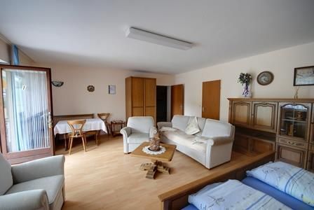 Ein helles Zimmer mit einem gemütlichen Wohnbereich. Es gibt eine Sitzecke, einen Tisch und ein paar Schränke.