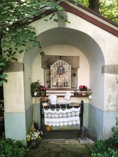 Eine kleine Kapelle mit einem bogenförmigen Eingang und Blumen. Der Raum ist geschmückt mit einer Fensterfront und einer Tischdecke.