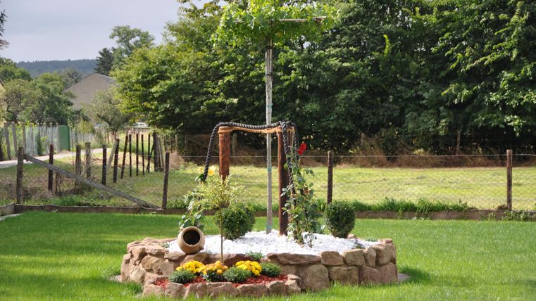 Ein schöner Garten mit einem runden Steinhaufen und einem kleinen Baum in der Mitte. Umgeben von einer grünen Wiese und einem Zaun.