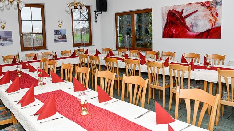 Ein festlich gedeckter Tisch in einem einladenden Raum. Rote Servietten und Tischdecken dekorieren die Tische für eine besondere Veranstaltung.