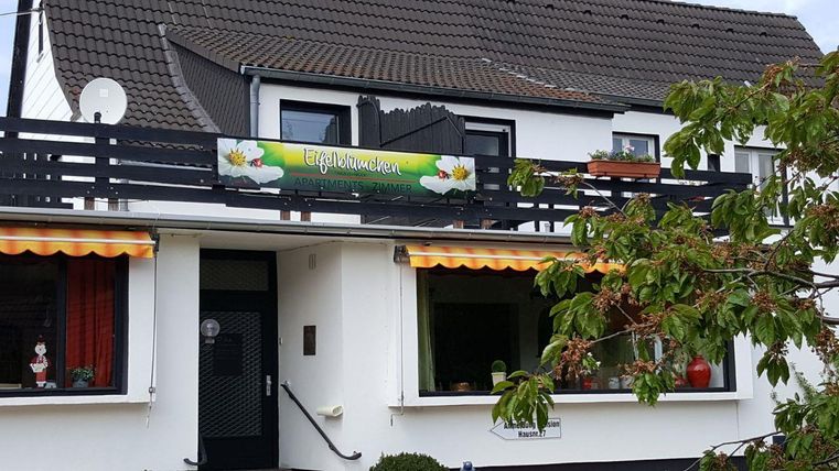 Ein hübsches Haus mit einem Balkon und einem Schild "Töpfereien". Vor den Fenstern sind bunte Vorhänge und Pflanzen.