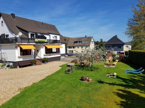Ein schönes Mehrfamilienhaus mit einem gepflegten Garten. Im Hintergrund sind weitere Wohnhäuser zu sehen.