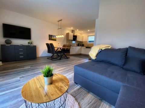 Ein modernes Wohnzimmer mit einem gemütlichen Sofa und einem runden Tisch. Im Hintergrund ist ein Essbereich mit einer offenen Küche sichtbar.