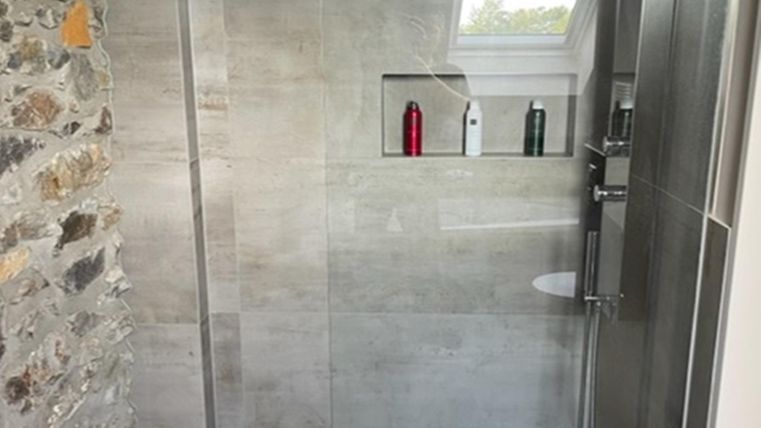 Eine moderne Dusche mit Glasschwingtür und eleganten Fliesen. In der Nische sind einige Pflegeprodukte sichtbar.