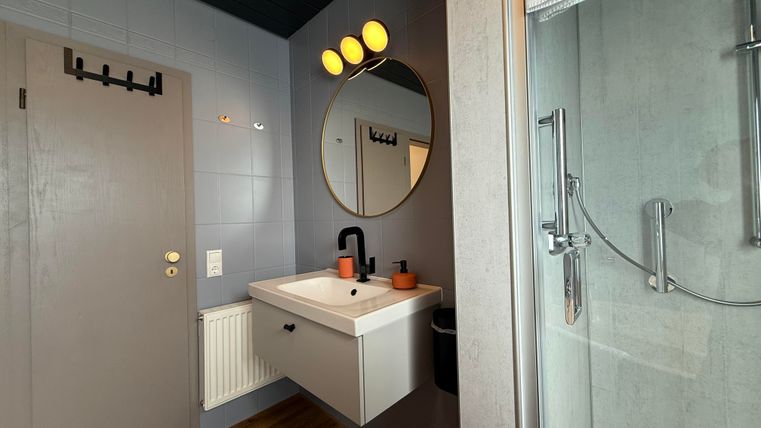 Ein modernes Badezimmer mit einem Waschbecken und einem runden Spiegel. Die Wände sind in dunklem Blau und Grau gehalten, und es gibt eine Dusche aus Glas.