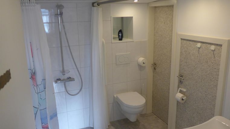 Ein modernes Badezimmer mit Dusche, WC und großen, hellen Fliesen. Es gibt einen Spiegel und eine einfache, funktionale Ausstattung.