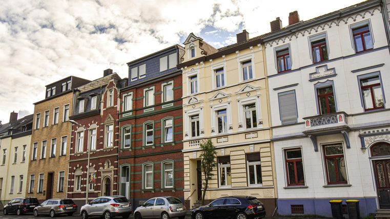 Eine Straße mit historischen Gebäuden in verschiedenen Farben. Parkende Autos ergänzen das Stadtbild.