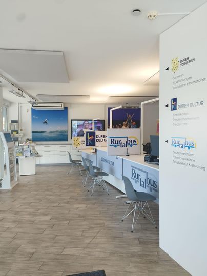 Ein modernes Büro mit hellem Innendesign und eleganten Möbeln. An den Wänden befinden sich Informationsmaterialien und Werbebanner.