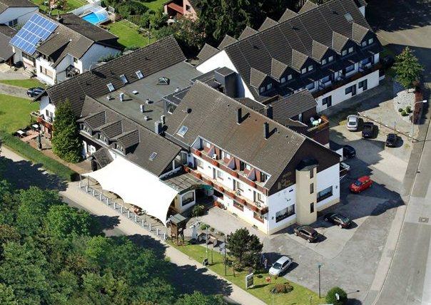 Ein Hotelgebäude mit mehreren Etagen und einem angrenzenden Parkplatz. Umgeben von Bäumen und einer ruhigen Nachbarschaft.