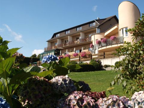 Ein modernes Gebäude mit Balkonen und bunten Blumenkästen. Im Vordergrund blühen Hortensien auf einer grünen Wiese.