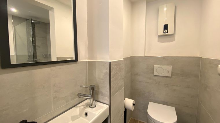 Ein modernes Badezimmer mit einer eleganten Toilette und einem kleinen Waschbecken. Die Wände sind hell und freundlich gefliest.