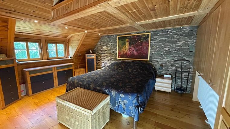 Ein gemütliches Schlafzimmer mit Holzwänden und einem großen Bett. Der Raum hat große Fenster und eine Kunstmalerei an der Wand.