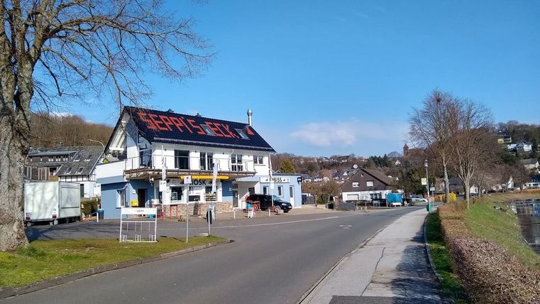 Eine Straße neben einem Fluss mit einem Gebäude auf der linken Seite. Das Gebäude hat ein rotes Schild mit der Aufschrift "Gerry's Grill".