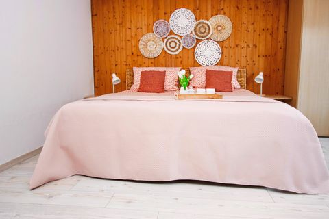 Ein gemütliches Schlafzimmer mit einem großen Bett und einem Holzpanel. Die Wände sind mit dekorativen Körben geschmückt und eine kleine Blumenvase steht auf dem Nachttisch.