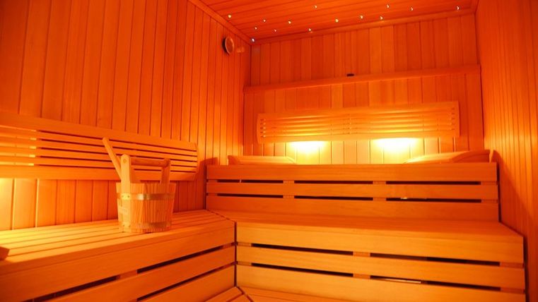 Eine gemütliche Sauna mit Holzverkleidung und sanfter Beleuchtung. Im Vordergrund steht ein Eimer mit Saunakellen.