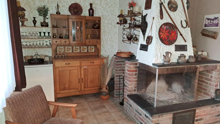 Ein gemütlicher Wohnraum mit einem offenen Kamin und rustikalen Dekorationen. Links steht ein Holzschrank, der mit verschiedenen keramischen Gegenständen und Pflanzen geschmückt ist.