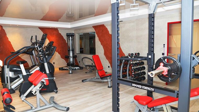Ein modernes Fitnessstudio mit verschiedenen Trainingsgeräten. Die Ausstattung umfasst Hanteln, Laufmaschinen und eine Kraftstation.