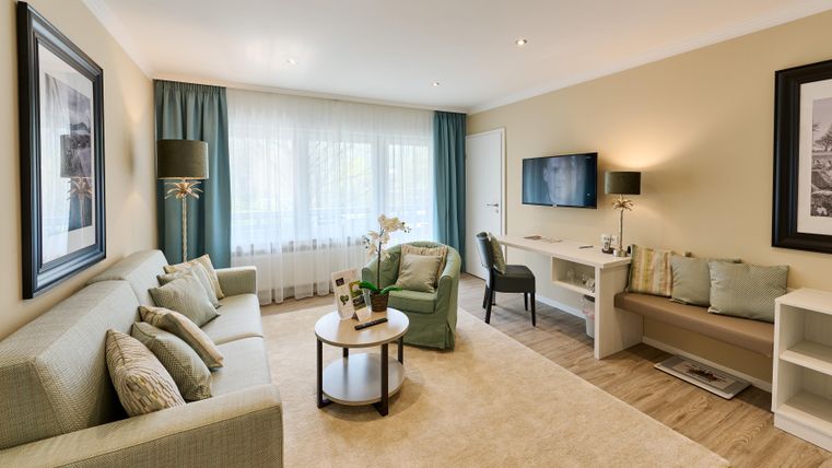 Ein modernes Wohnzimmer mit hellen Wänden und gemütlicher Einrichtung. Es gibt ein Sofa, einen kleinen Tisch und einen Fernseher.