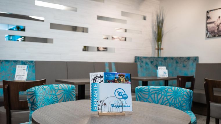 Ein gemütliches Café mit bunten Stühlen und modernen Wänden. Auf dem Tisch steht eine Eiskarte, die das entspannte Ambiente unterstreicht.