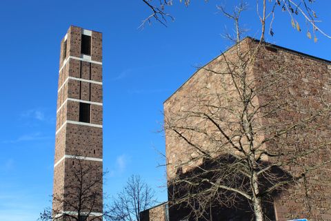 Ein modernes Gebäude mit einer hohen, gebäudeartigen Struktur und einem schmalen Turm. Der klare blaue Himmel und die kahlen Bäume verleihen der Szene eine ruhige Atmosphäre.