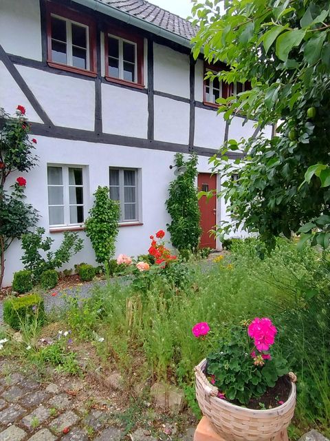 Ein traditionelles Fachwerkhaus mit einem gepflegten Garten. Bunte Blumen und grüne Pflanzen schmücken den Eingang.