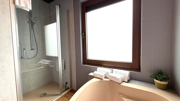 Ein modernes Badezimmer mit einer Dusche und einer Badewanne. Der große Fenster sorgt für viel Tageslicht.