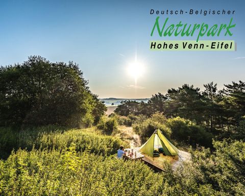 Ein wunderschöner Ausblick auf den Naturpark Hohes Venn-Eifel mit einer grünen Zeltlandschaft. Die Sonne geht am Horizont auf und beleuchtet die Umgebung.
