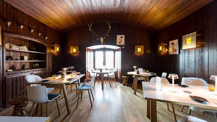 Ein gemütliches Restaurant mit dunklen Holzwänden und einem warmen Ambiente. Tische sind elegant gedeckt und mit modernen Stühlen ausgestattet.