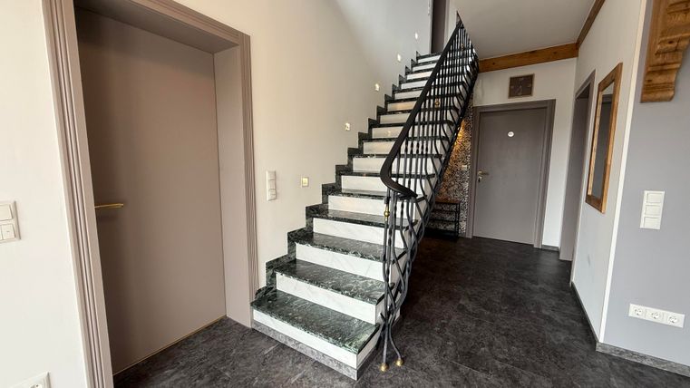Ein moderner Eingangsbereich mit einer eleganten Treppe. Die Wände sind in neutralen Farben gehalten und der Boden ist dunkel gefliest.