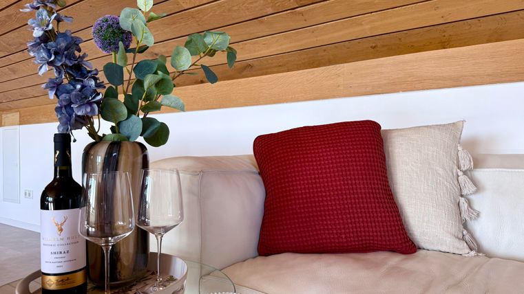 Ein stilvoller Wohnbereich mit einer Couch, einem roten Kissen und einer Vase mit Blumen. Auf dem Tisch stehen eine Flasche Wein und zwei Weingläser.