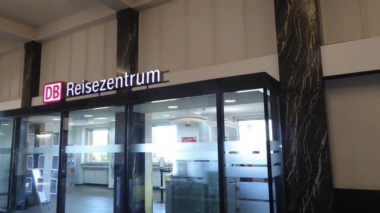 Ein Reisezentrum der Deutschen Bahn mit großen Glasfenstern. Der Bereich ist modern gestaltet und wirkt einladend.