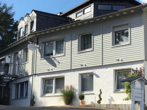 Ein moderner Gebäudekomplex mit einer Kombination aus hellgrauer und weißer Fassade. Der Himmel ist blau und es gibt einige Pflanzen am Gebäude.